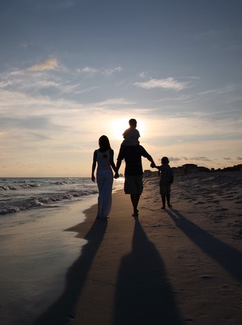 husband and wife walking on beach with their children during sunset